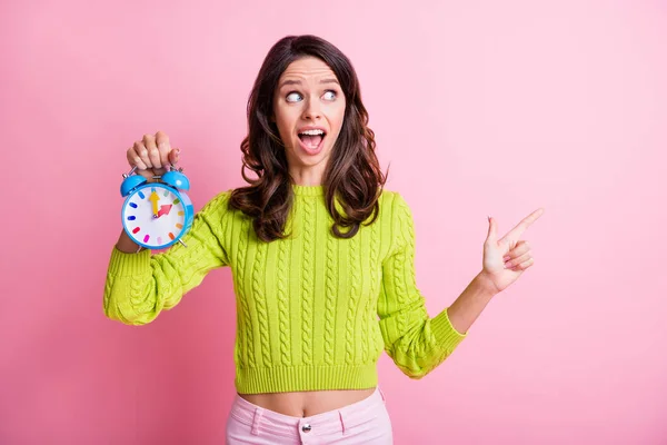 Foto de dama ondulada impresionada usar suéter verde apuntando con el dedo espacio vacío sosteniendo alarma aislado color rosa fondo — Foto de Stock