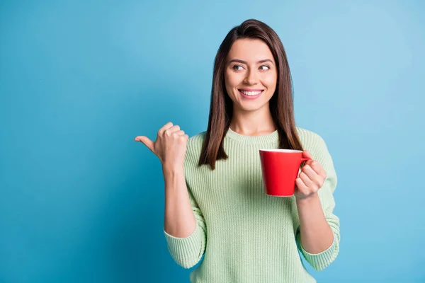 Foto de dedo de la muchacha positiva espacio vacío mantenga taza de café con leche desgaste suéter verde aislado sobre fondo de color azul — Foto de Stock
