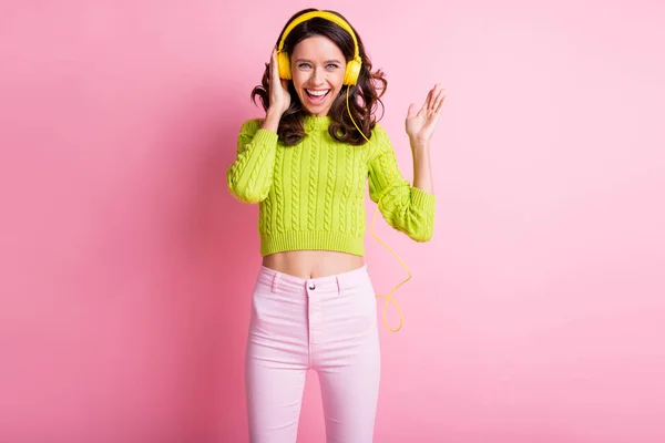 Foto de hermosa mujer rizada vestida verde pullover bailando escuchando música auriculares aislados color rosa fondo — Foto de Stock
