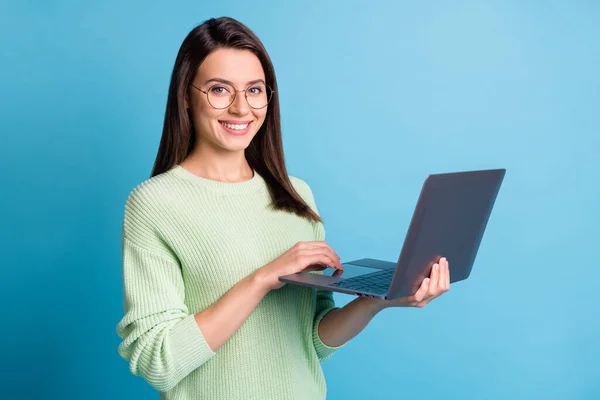 Φωτογραφία του θετικού κοριτσιού που εργάζονται σε φορητό υπολογιστή φορούν πράσινο πουλόβερ απομονώνονται σε μπλε χρώμα φόντο — Φωτογραφία Αρχείου