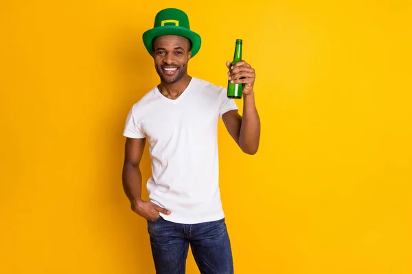 Zdrowie kumpli. Photo of attractive dark skin guy hold beer beverage bottle students party saint Patrick day wear casual white t-shirt isolated bright vivid yellow color background — Zdjęcie stockowe