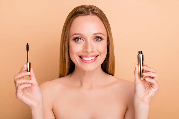 Primer plano ver retrato de bonito brillo encantador alegre desnuda chica desnuda sosteniendo en las manos nuevo producto novedad cepillo tubo rímel tono look partido preparación aislado sobre fondo beige pastel — Foto de Stock