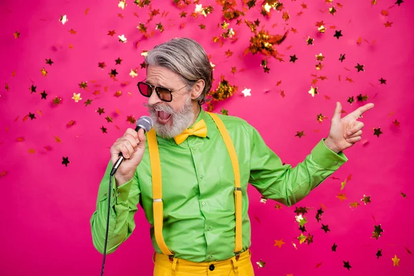 Foto av roligt vitt hår farfar klubb fest kylande sång karaoke använda mikrofon konfetti falla slitage sol specs grön skjorta gula hängslen isolerad ljus rosa färg bakgrund — Stockfoto