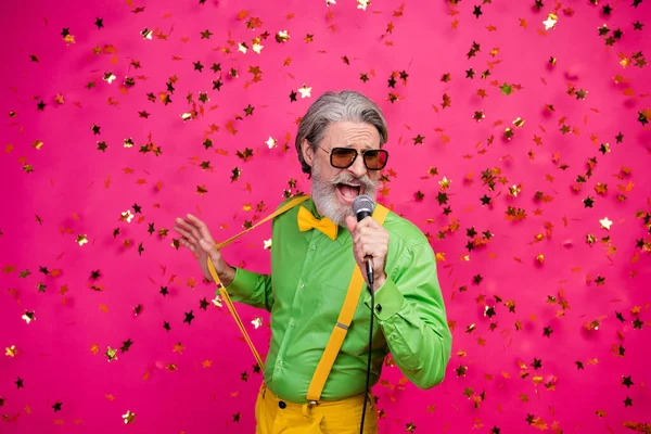 Foto di divertente invecchiato nonno club partito canto karaoke microfono coriandoli caduta eccitato cantante indossare sole specs verde camicia giallo bretelle cravatta isolato lucentezza rosa colore sfondo — Foto Stock