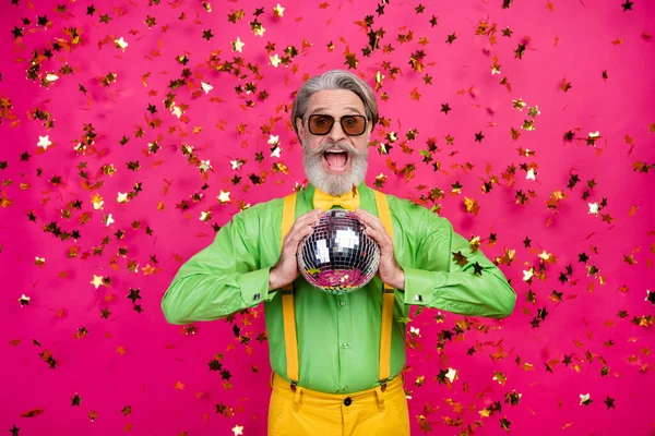 Foto van grappige opa party club confetti vallen opgewonden open mond houden gloeiende disco bal dragen zon specs groen shirt geel bretels strik geïsoleerde glans roze kleur achtergrond — Stockfoto