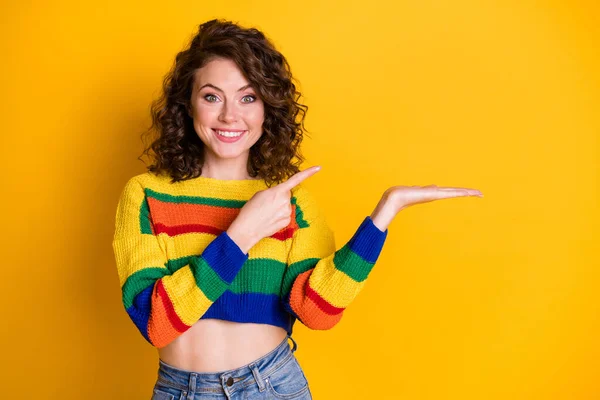 Foto der schönen jungen Dame direkt Finger Handfläche halten leeren Raum zahmes Lächeln tragen gestreiften Pullover isoliert gelben Hintergrund — Stockfoto