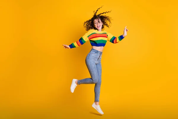 Фотографія повної довжини смішної стрибки леді в повсякденному кольоровому светрі, що танцює, вказуючи на порожній простір ізольованого жовтого кольору фону — стокове фото