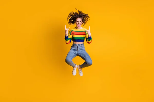 Foto de longitud completa de la mujer saltando divertida vestida sudadera colorida casual que muestra el signo de roca dura aislado fondo de color amarillo — Foto de Stock