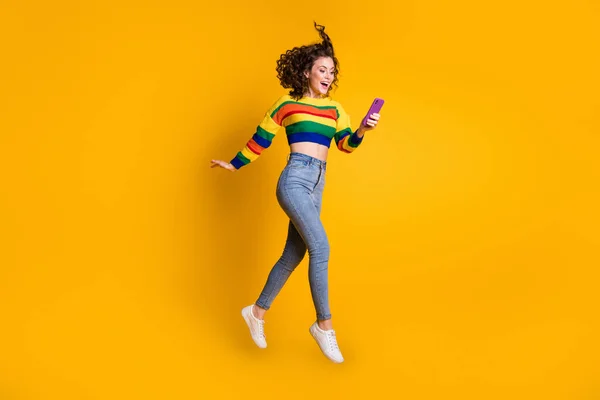 Foto de comprimento total de pular senhora blogger vestindo casual colorido suéter telefone mãos braços isolado cor amarela fundo — Fotografia de Stock