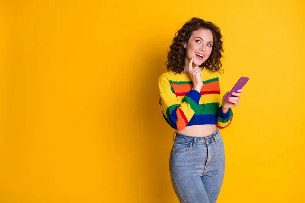 Foto av glad söt ung kvinna stå drömmande ser tomt utrymme hålla telefonen isolerad på gul bakgrund — Stockfoto
