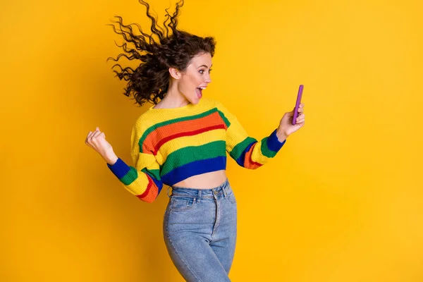 Foto de hooray bastante rizado chica del pelo mirada teléfono desgaste pantalones vaqueros brillantes aislados sobre brillo amarillo color fondo — Foto de Stock