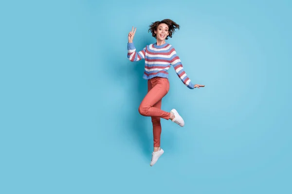 Foto de cuerpo entero del tamaño de la longitud de saltar encima del estudiante femenino mostrando gesto v-signo dos dedos aislados en el fondo de color azul vibrante —  Fotos de Stock