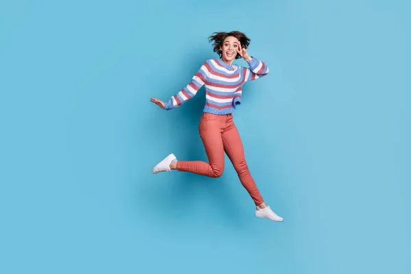 Фотография прыгающей высокой девушки в полный рост, показывающей жест V-знака двумя пальцами, изолированными на ярком синем цветовом фоне — стоковое фото