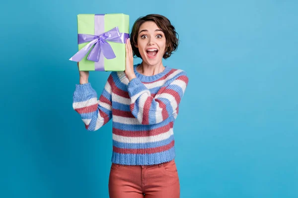 Retrato fotográfico de una chica sorprendida sosteniendo presente cerca de la oreja con la boca abierta aislada sobre un fondo de color azul vivo —  Fotos de Stock