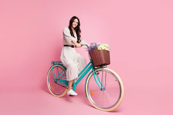 Ganzkörpergröße Foto einer Studentin in weißem Outfit Fahrrad fahren mit Blumen lächeln glücklich isoliert pastellrosa Hintergrund — Stockfoto