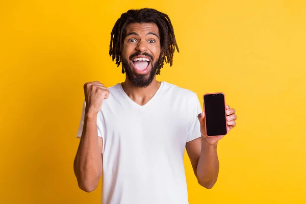 Foto van zwarte man hold telefoon demonstreren touchscreen lege ruimte raise vuist open mond slijtage witte t-shirt geïsoleerde gele kleur achtergrond — Stockfoto