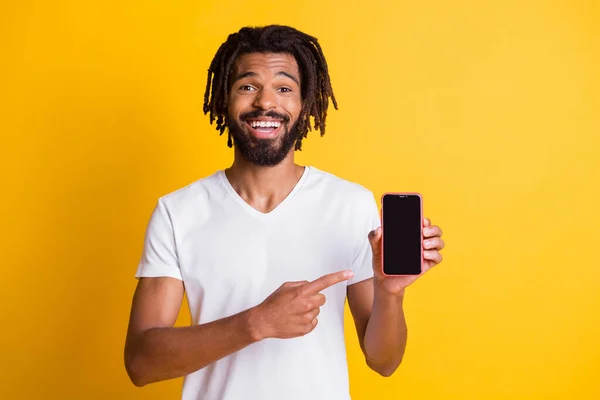 Foto de tipo negro barba rastas indican sujeción del dedo que muestra teléfono pantalla táctil espacio vacío desgaste blanco camiseta aislado color amarillo fondo — Foto de Stock