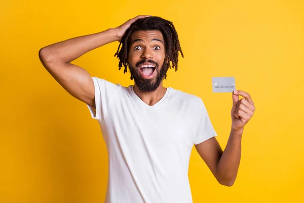 Photo of black guy hand head hold credit card open mouth wear white t-shirt odizolowany żółty kolor tło — Zdjęcie stockowe