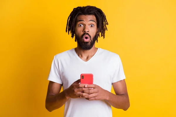 Foto van zwarte man houden telefoon kijken camera geschokte uitdrukking dragen witte t-shirt geïsoleerde gele kleur achtergrond — Stockfoto