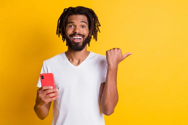 Foto van grappige verbaasd donkere huid man houden telefoon sturen vinger lege ruimte nieuwigheid geïsoleerde gele kleur achtergrond — Stockfoto