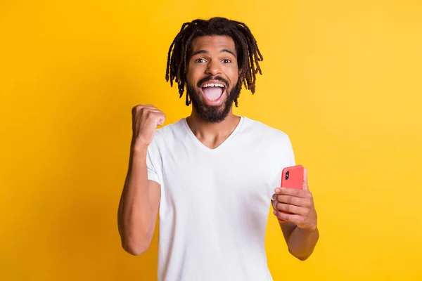 Foto van grappige donkere huid jongen houden telefoon vieren win slijtage t-shirt geïsoleerde gele kleur achtergrond — Stockfoto