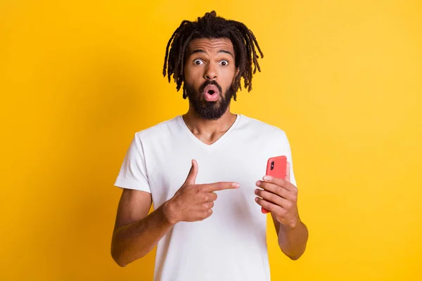 Foto van verbaasd donkere huid guy houden telefoon directe vinger scherm upgrade interface slijtage t-shirt geïsoleerde gele kleur achtergrond — Stockfoto