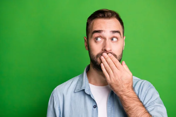 Retrato de tipo asustado labios de la mano mirada espacio vacío desgaste camisa azul aislado sobre fondo de color verde vibrante — Foto de Stock