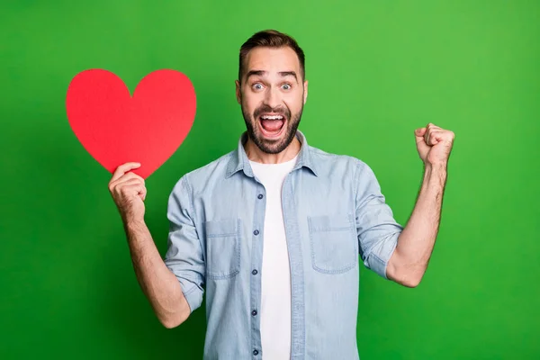 Retrato de hooray cara segurar vermelho coração mão punho desgaste azul camisa isolada no vibrante verde cor fundo — Fotografia de Stock