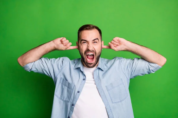 Retrato de hombre enojado manos orejas gritar usar camisa azul aislado en fondo de color verde vibrante — Foto de Stock