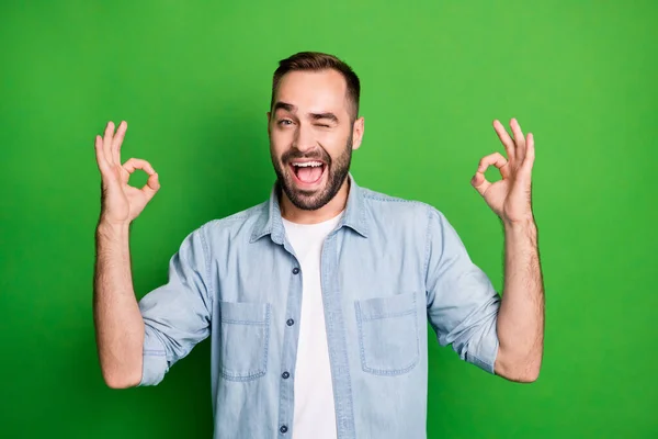 Retrato de chico fresco muestran signo okey parpadeo desgaste camisa azul aislado sobre fondo de color verde vibrante — Foto de Stock