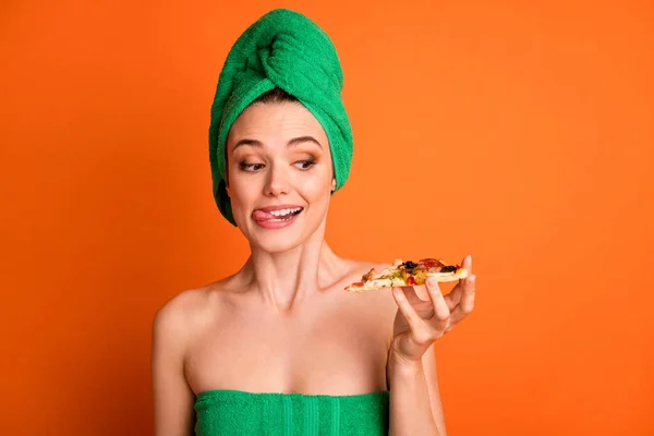 Photo portrait of woman holding in one hand looking at pizza slice licking lips isolated on vivid orange colored background