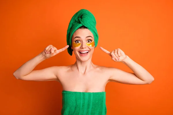 Portrait photo d'une femme pointant du doigt des patchs dorés portant une serviette de bain verte isolée sur fond orange vif — Photo