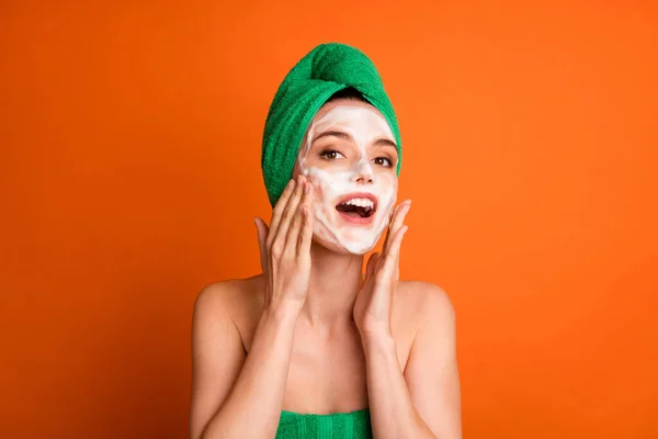 Φωτογραφία από γλυκό λαμπερό κυρία φορούν πράσινη πετσέτα κεφάλι εφαρμόζοντας σαπούνι δύο ζυγωματικά χέρια απομονωμένο πορτοκαλί χρώμα φόντο — Φωτογραφία Αρχείου