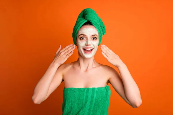 面白い驚きの女性の写真は、マスク顔の腕を適用する緑色のタオルの頭を着用孤立オレンジの背景 — ストック写真