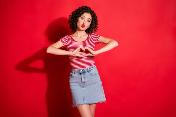 Cilveli genç bir kadının fotoğrafı çizgili kıyafet giymiş dudaklar somurtmuş parmaklar gösteriyordu kalp izole kırmızı arka plan — Stok fotoğraf