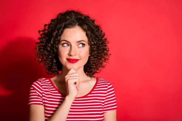 Photo de jolie jeune femme bouclée rêveuse porter casual rayé tenue bras menton regardant vide espace isolé couleur rouge fond — Photo