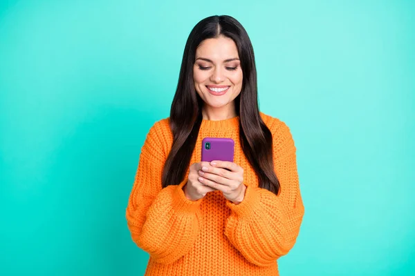 Foto van charmante dame houden telefoon kijken scherm tand glimlach dragen oranje trui geïsoleerde teal kleur achtergrond — Stockfoto