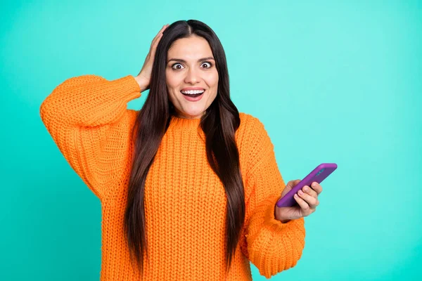 Foto von überrascht Mädchen halten Smartphone-Look Kamera Handfläche Kopf tragen orange Pullover isoliert türkisfarbenen Hintergrund — Stockfoto