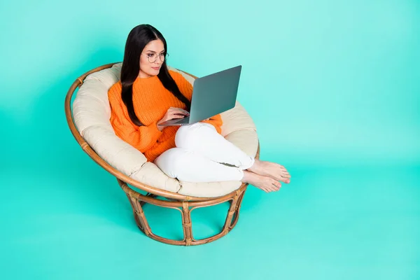 Kendine güvenen bir kızın fotoğrafı koltuğa otur netbook tut gözlük giy turuncu süveter giy izole edilmiş gök mavisi arkaplan — Stok fotoğraf