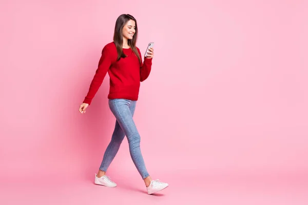 Foto de perfil de comprimento total de menina bonita passo segurar telefone olhar tela desgaste vermelho pulôver jeans tênis isolado cor-de-rosa fundo — Fotografia de Stock