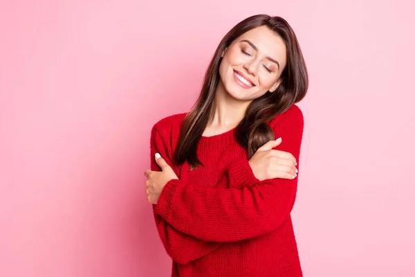 Фотографічний портрет красивої красивої дівчини, яка посміхається закритими очима, обіймаючи себе, насолоджуючись червоним вбранням, ізольованим на рожевому кольорі — стокове фото