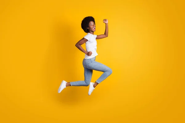 Tamanho do corpo de comprimento total foto de estudante alegre feliz do sexo feminino com a pele preta saltando alto correndo rápido gritando alto isolado no fundo de cor amarelo brilhante — Fotografia de Stock