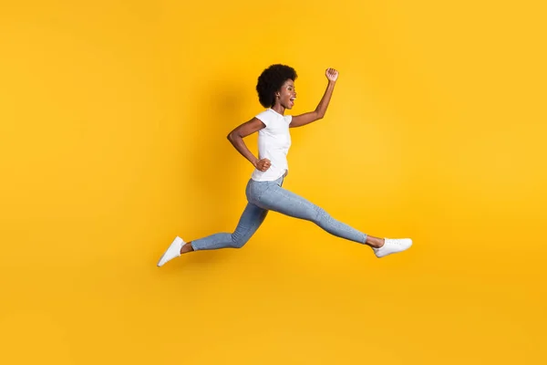 Tamanho do corpo de comprimento total foto de jovem millennial feminino com pele preta saltando alto correndo rápido torcendo isolado no fundo de cor amarelo brilhante — Fotografia de Stock