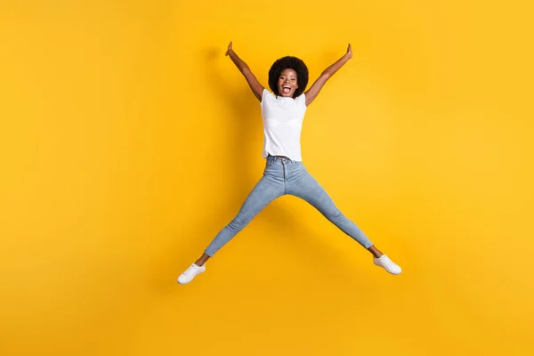 Фотография в полный рост изумленной удивленной девушки с черной кожей, прыгающей высоко притворяющейся звездой, смеющейся изолированной на ярко-желтом цветовом фоне — стоковое фото