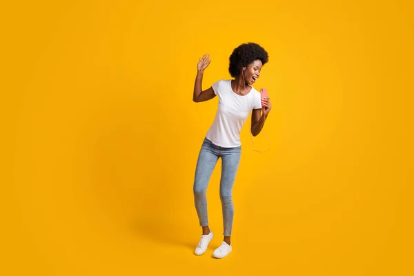 Full length body size φωτογραφία του funky θηλυκό hipster με μαύρο δέρμα ακούγοντας μουσική χορεύοντας τραγούδι κρατώντας smartphone απομονώνονται σε φωτεινό κίτρινο χρώμα φόντο — Φωτογραφία Αρχείου