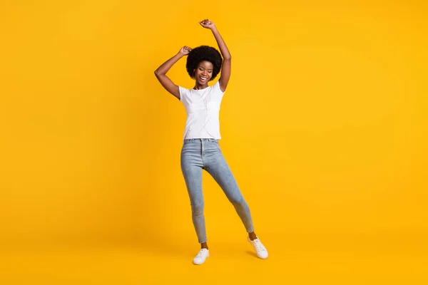 Ganzkörpergröße Foto von lächelnden Mädchen mit schwarzer Haut hören Lied tanzen halten die Hände nach oben isoliert auf leuchtend gelben Farbhintergrund — Stockfoto
