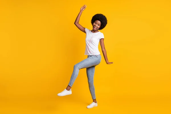 Tamanho total do corpo foto de menina alegre com a pele preta ouvindo melodia dançando com fones de ouvido laranja sorrindo rindo isolado no fundo de cor amarelo brilhante — Fotografia de Stock