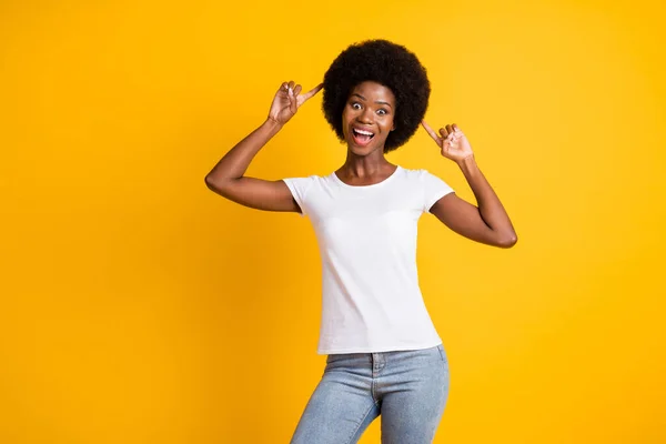 Foto porträtt av galen afrikansk amerikansk kvinna pekar två fingrar på hennes hår med öppen mun bär vit t-shirt isolerad på levande gul bakgrund — Stockfoto