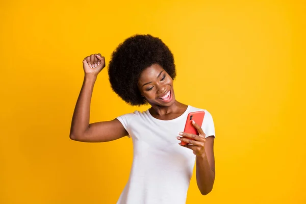 Foto portret van jonge vrouw vieren overwinning met een vuist omhoog het dragen van casual wit t-shirt geïsoleerd op levendige geel gekleurde achtergrond — Stockfoto