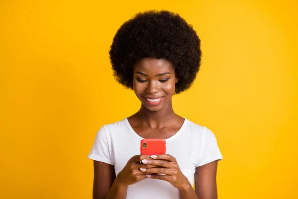 Foto portret van meisje met telefoon in twee handen glimlachend dragen casual wit t-shirt geïsoleerd op levendige geel gekleurde achtergrond — Stockfoto